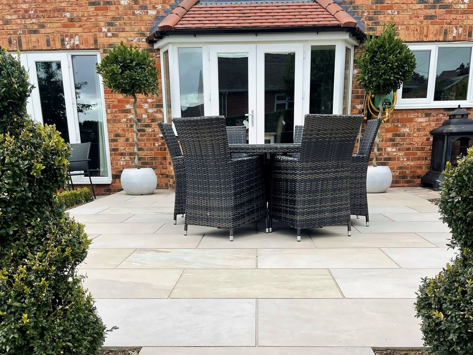 Pale stone patio outside French doors on a brick house, with topiary and outdoor dining