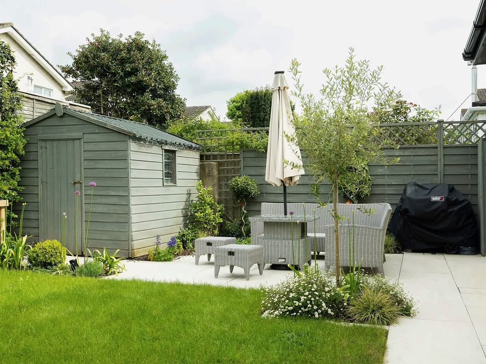 Back garden with a lawn, pale paving, a timber shed and grey fencing