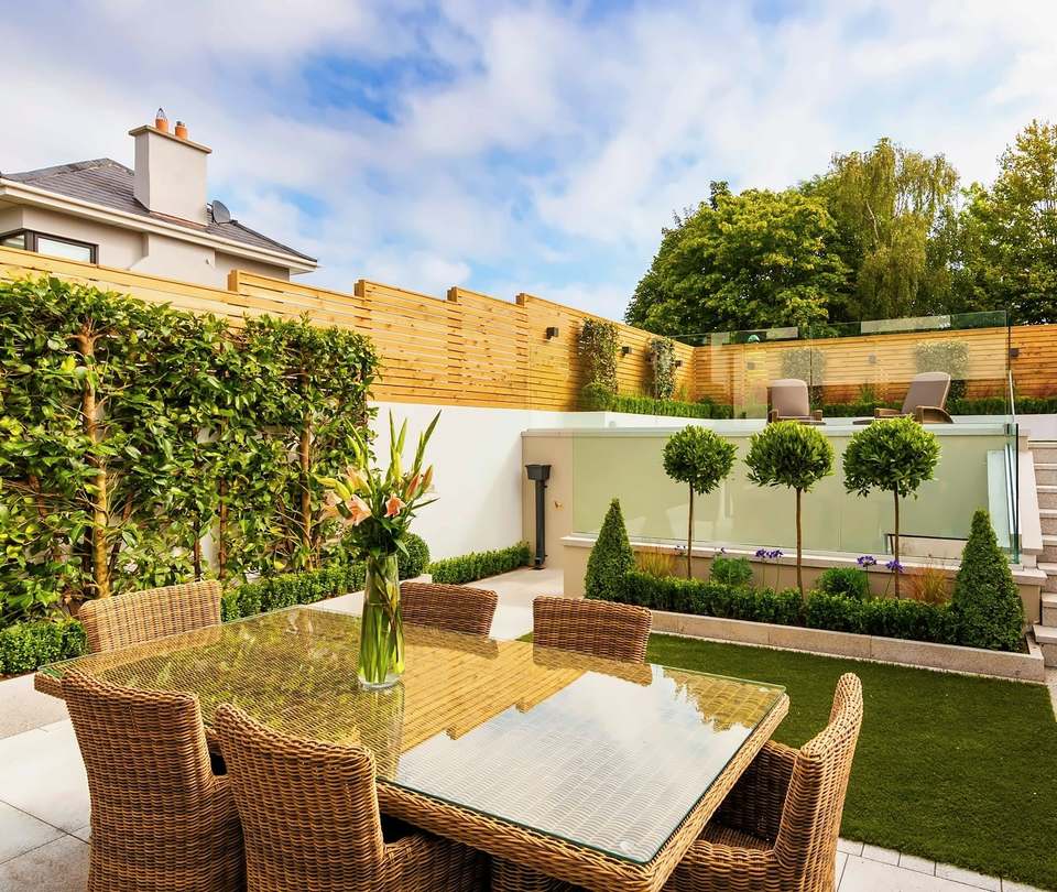Tiered garden with a dining patio, steps up to a lawn, clipped hedging and timber fencing