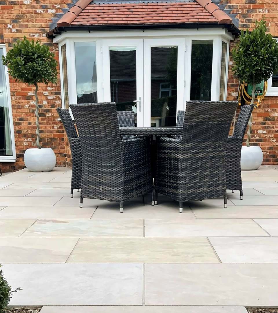 Pale stone patio outside French doors on a brick house, with topiary and outdoor dining